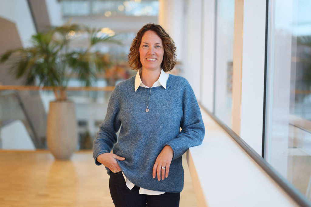 Porträtt kvinna med brunt hår och blå tröja över vit skjorta