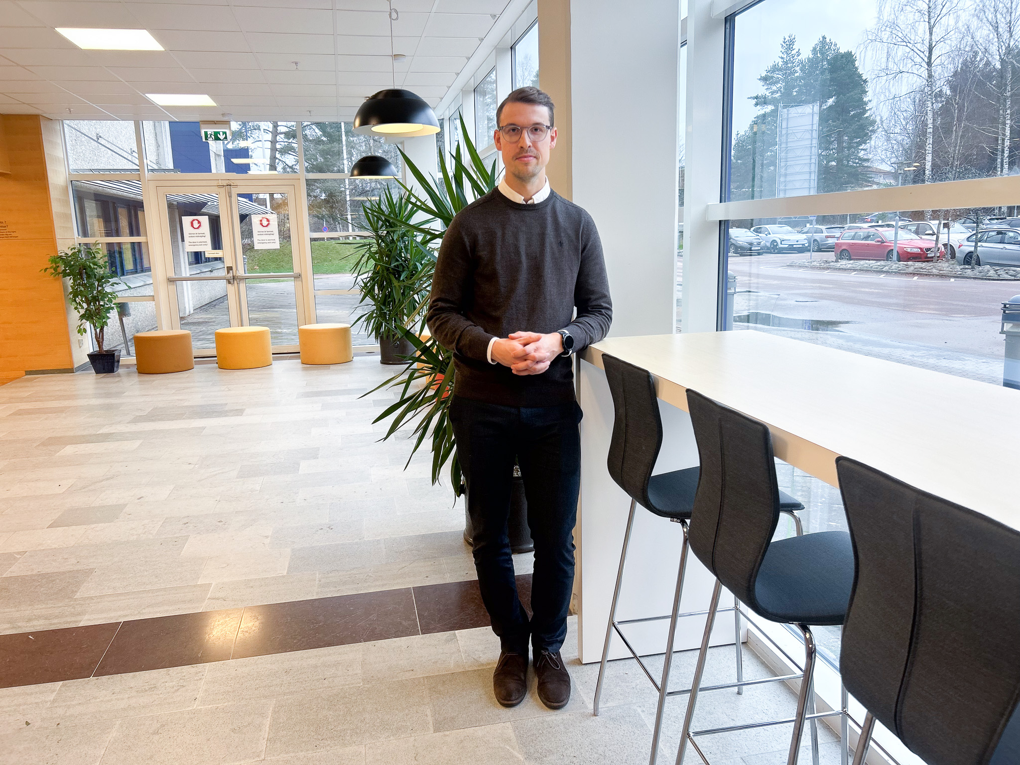 Man i mörka kläder som står innomhus lutad mot ett bord.